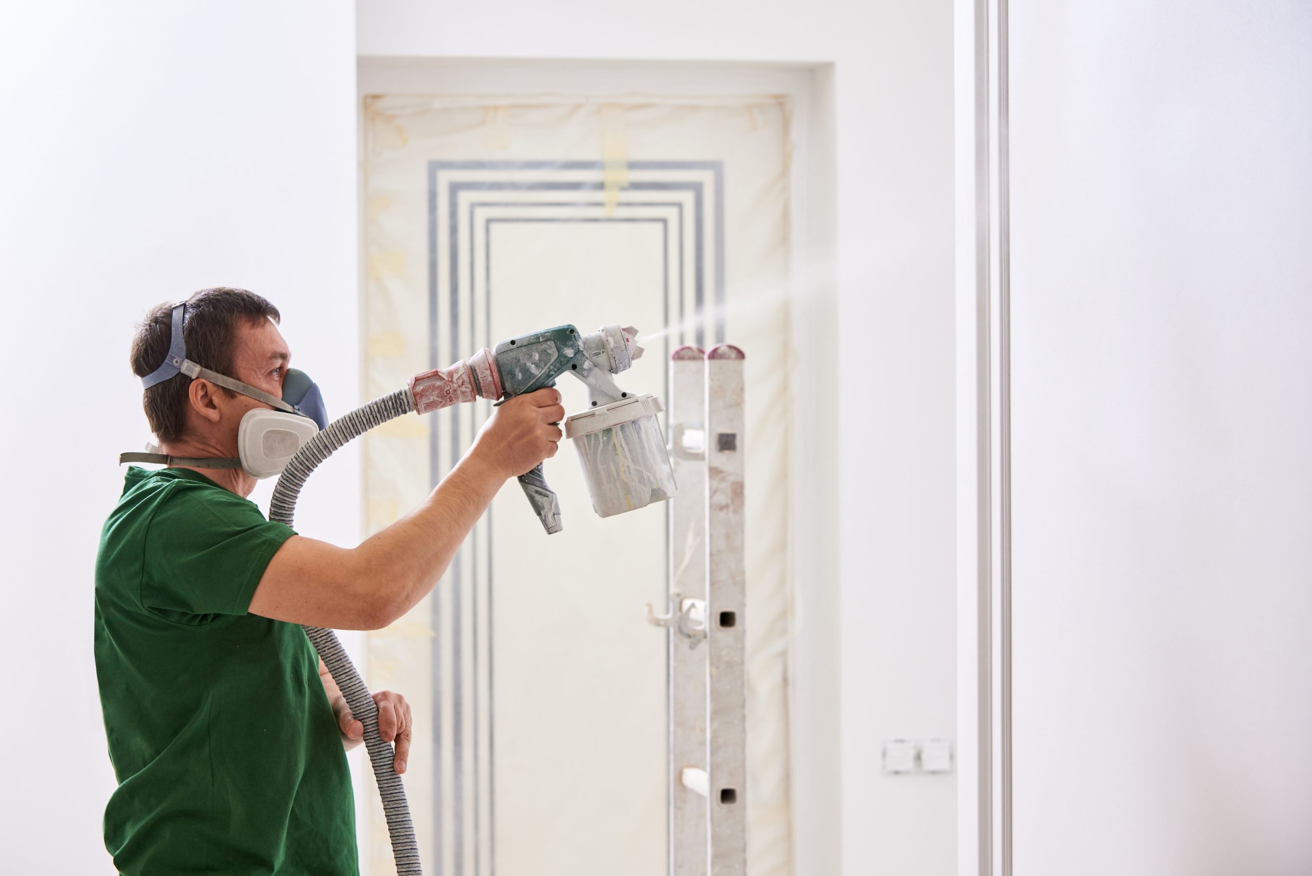 Condtruction worker painting wall with spray gun in white color.